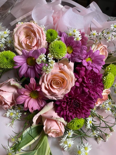 A vibrant floral bouquet featuring soft pink roses with tightly layered petals, complemented by bright purple daisy-like flowers with distinct central disks, and small white daisies with yellow center