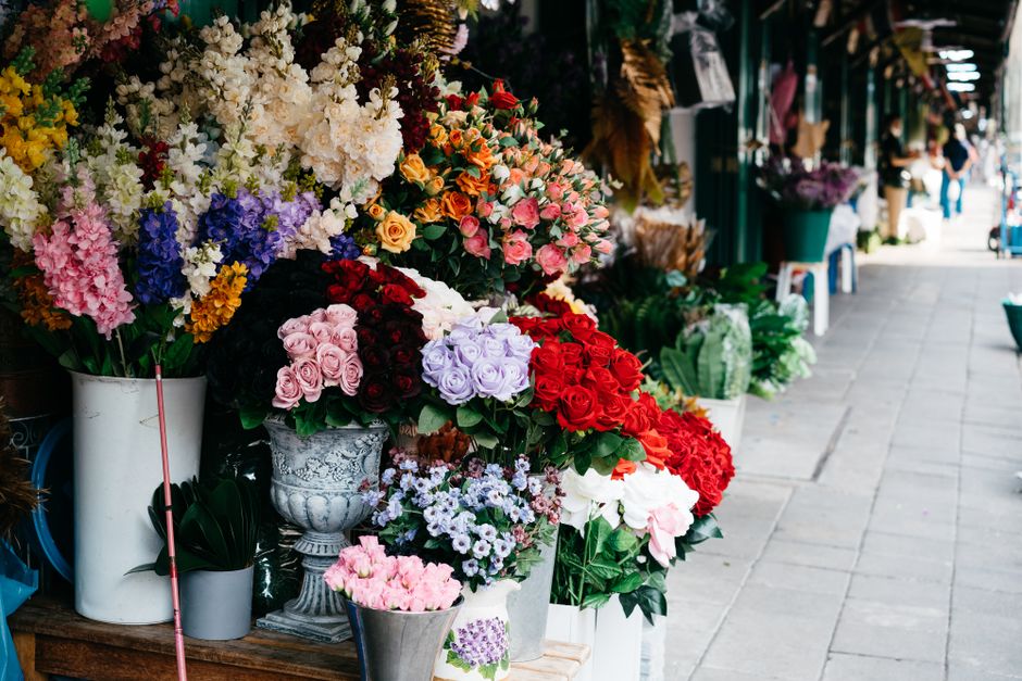 A vibrant display of fresh floral arrangements outside a flower shop, featuring an assortment of bouquets with roses, carnations, and other blooms in shades of pink, red, purple, white, and yellow. Th