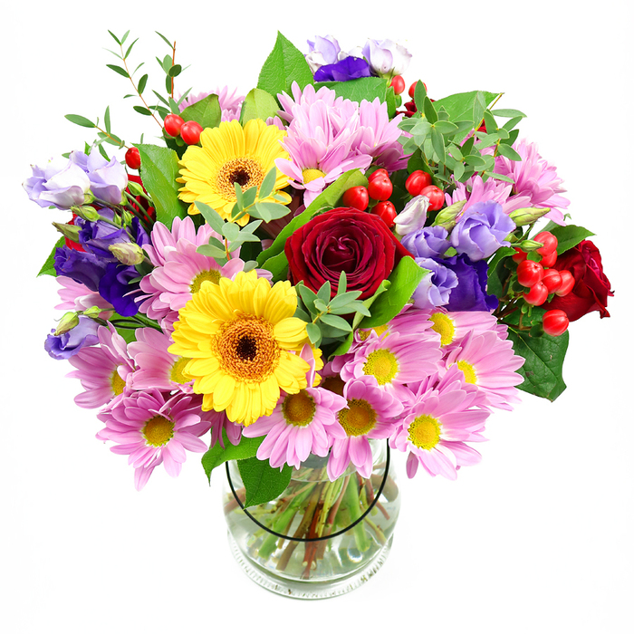 A vibrant, multi-coloured bouquet fills a clear glass vase, captured against a clean white background that highlights its lively mix of tones and textures. At its core are rich, deep red roses, their velvety petals layered in elegant spirals that create a sense of depth and classic sentiment, as though they were chosen to say what words sometimes cannot. Nestled close by, golden yellow gerbera daisies with dark brown-orange centres shine brightly, their broad, regular petals forming open faces that seem to radiate friendliness and optimism. The bouquet's generous shape is completed by clusters of soft pink and lilac daisies or chrysanthemums, each blossom composed of many slender petals surrounding small yellow hearts, adding a cushion of gentle colour that surrounds and supports the stronger hues. Moving through the arrangement are slender stems of lisianthus in varying shades of purple and lavender; some buds are still softly closed, while others open into bell-shaped, slightly ruffled flowers, lending the bouquet a layered, almost flowing movement. Between the petals, small groups of rounded red hypericum berries sit like glossy jewels, adding both texture and a modern flair. All of this is woven through with fresh greenery, from solid, deeper green leaves that give structure and stability, to finer, lighter sprigs that arch and spill slightly, creating a natural, garden-picked effect reminiscent of the paths around Chislehurst Ponds or the leafy lanes near Camden Park Road. The clear glass vase reveals the cleanly cut stems, carefully arranged in fresh water, an understated detail that speaks of professional floristry. The overall mood is one of joyful celebration and warmth, a bouquet that could easily become the highlight of a birthday, anniversary, or simple thinking of you delivery in and around Chislehurst.