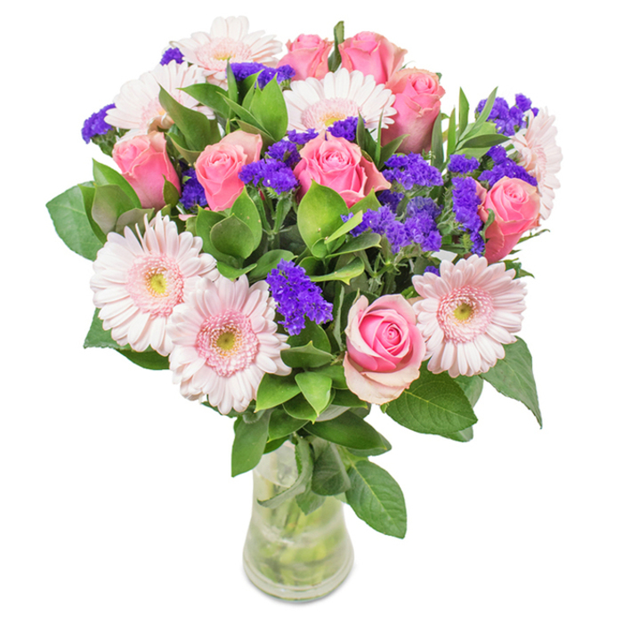 Set against the crisp background of a Chislehurst morning, this floral arrangement is a study in balance and beauty, masterfully presented in a crystal-clear vase. About seven to nine pink roses take centre stage, their spiralled petals in early bloom or poised to open fully, each carrying timeless elegance. These are paired with clusters of pale pink gerbera daisies, the large, radial heads and almost-white centers providing a soft textural counterpoint. Sprigs of vivid purple statice brighten the scene, offering bursts of colour interspersed among the softer tones and echoing the wildflowers found throughout Chislehurst's green spaces. A bed of deep green foliage cradles the display, conveying freshness and a sense of natural abundance, as if gathered from the paths of Chislehurst Woods. The transparent vase, with visible stems crossing through clear water, completes the arrangement's modern yet natural charm. Ideal as a birthday treat, an anniversary gift, or a refined decorative accent for a Chislehurst home, this bouquet speaks of celebration, affection, and carefully curated joy, reflecting the refined tastes and verdant surroundings of the area.